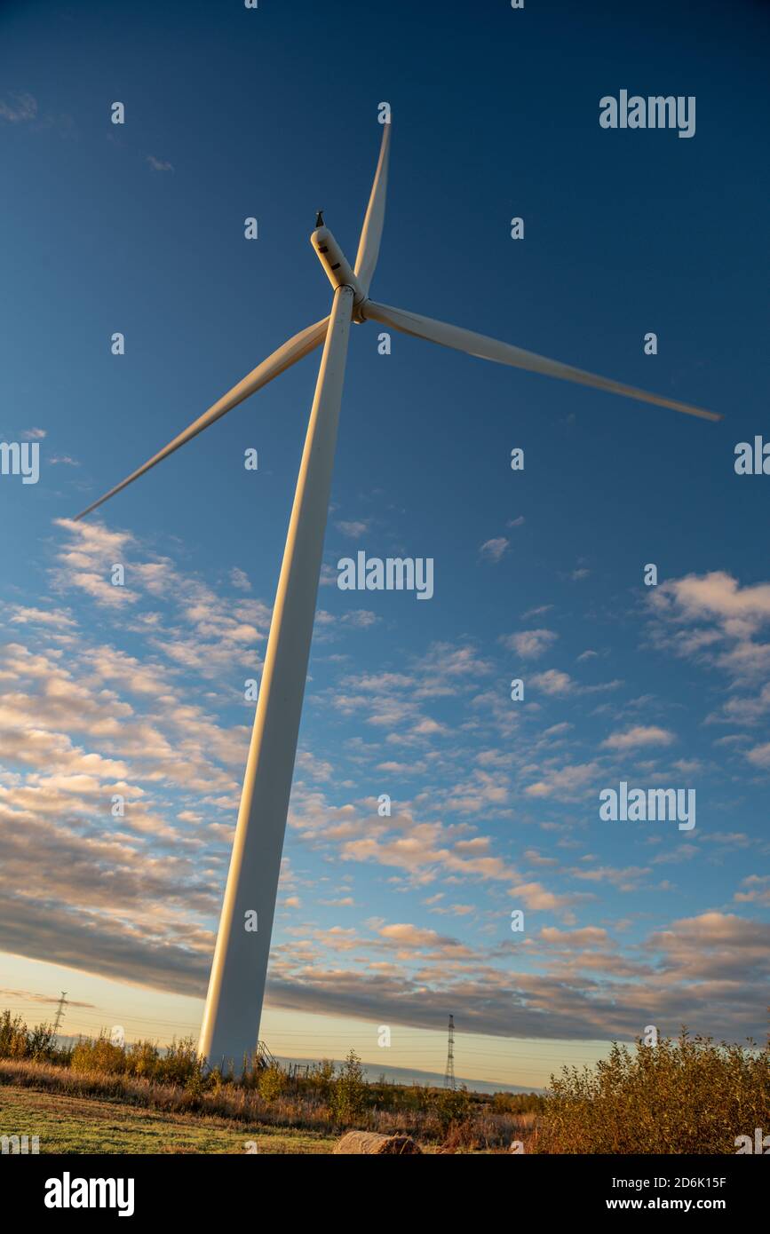 wind generator in white rotates on a background of blue sky with clouds and green grass on the ground Stock Photo