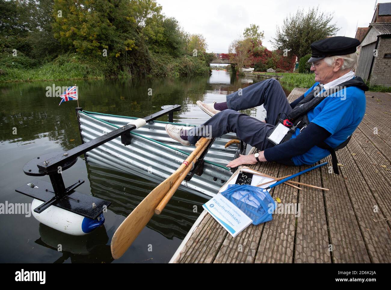 Michael Stanley, who is also known as 'Major Mick', 80, places a Union flag into the bow of his boat in Hunston, West Sussex, as he prepares to row along the Chichester canal in the home-made rowing boat, named the Tintanic. Major Mick, 80, is rowing along the Chichester canal in his home-made rowing boat, named the Tintanic, for a 100-mile charity challenge, rowing 3 miles at a time, to raise money for St Wilfrid's Hospice in Bosham. Stock Photo