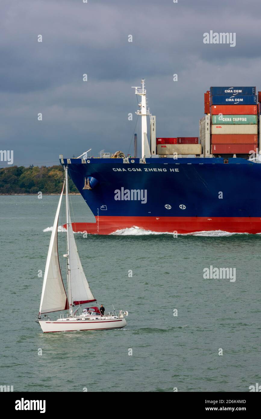 yacht sailing close to the bow of a large container ship in the thorn channel on the approach to the port of southampton docks in the solent shipping. Stock Photo