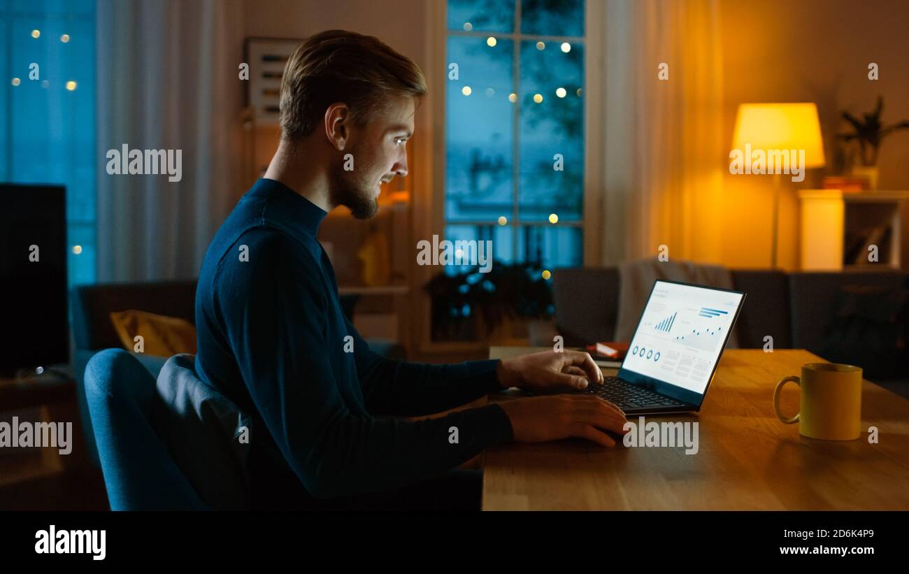 Evening at Home: Man Works on a Laptop Showing Statistical Infographic. Cozy Living Room with Warm Lights. Stock Photo