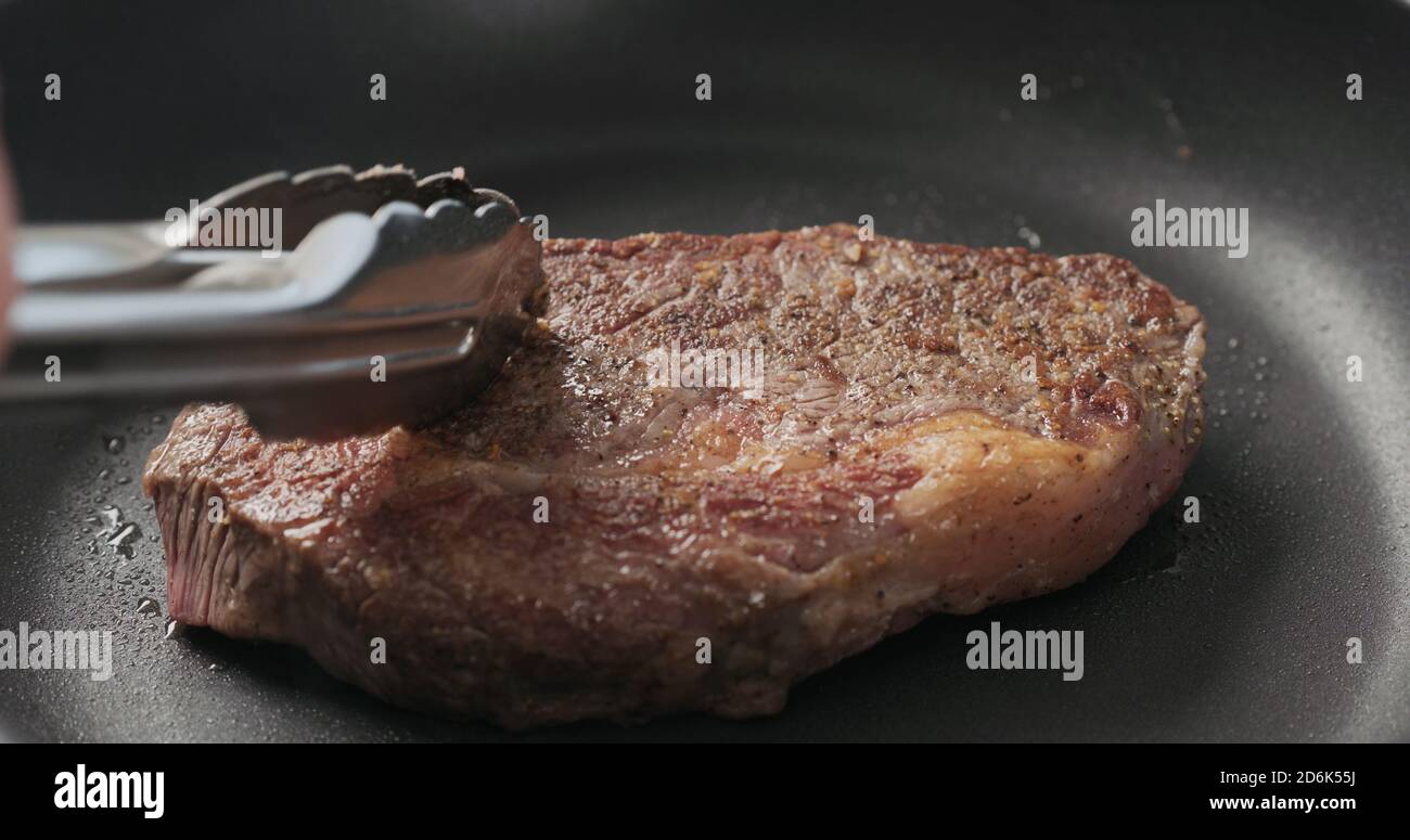 Closeup shot of man hands flip ribeye steak on non stick pan with steel