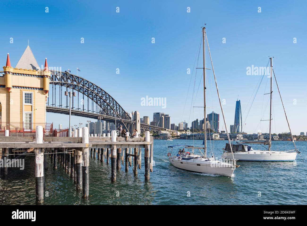 With the Sydney Harbour Bridge in the background a sleek yacht motors into Lavender Bay past Luna Park, Milsons Point, Australia Stock Photo