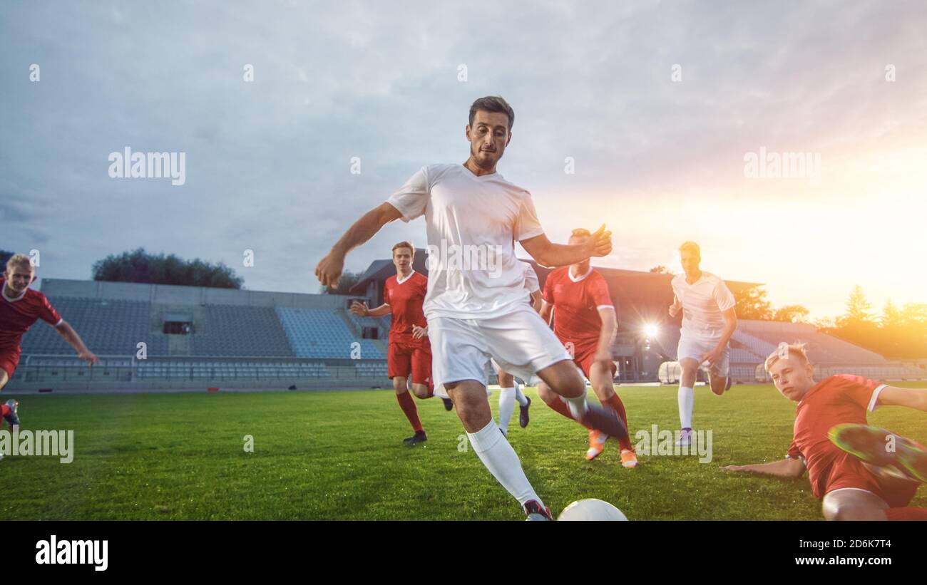 Professional Soccer Player Outruns Members of Opposing Team and Kicks Ball to Score Goal. Soccer Championship on a Stadium. Shot with Warm Sunlight in Stock Photo