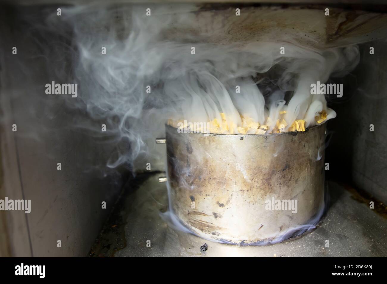 Metal pot with sawdust and smoke in an industrial oven for smoking fish