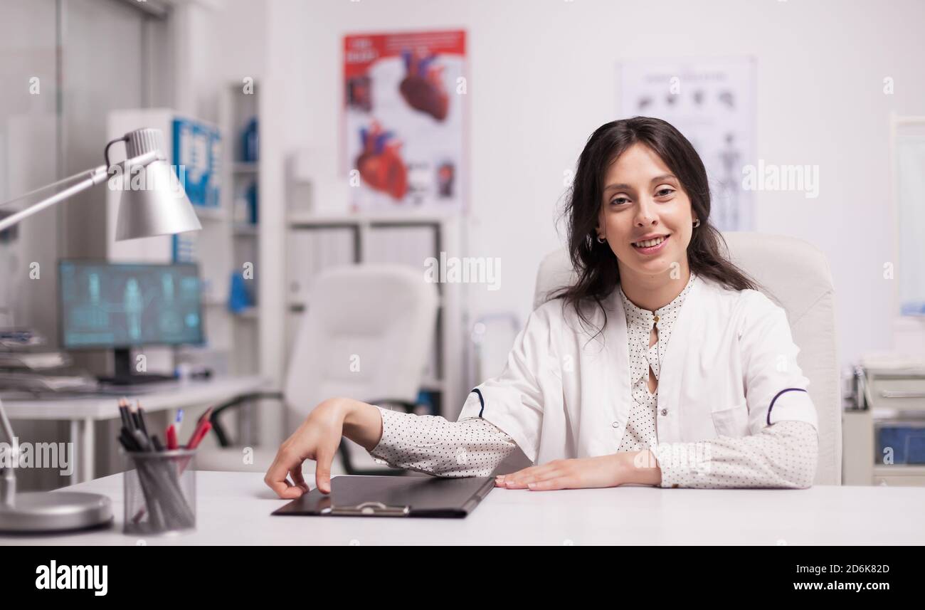 Cheerful attractive woman doctor in hospital office wearing white coat smiling to camera. Stock Photo