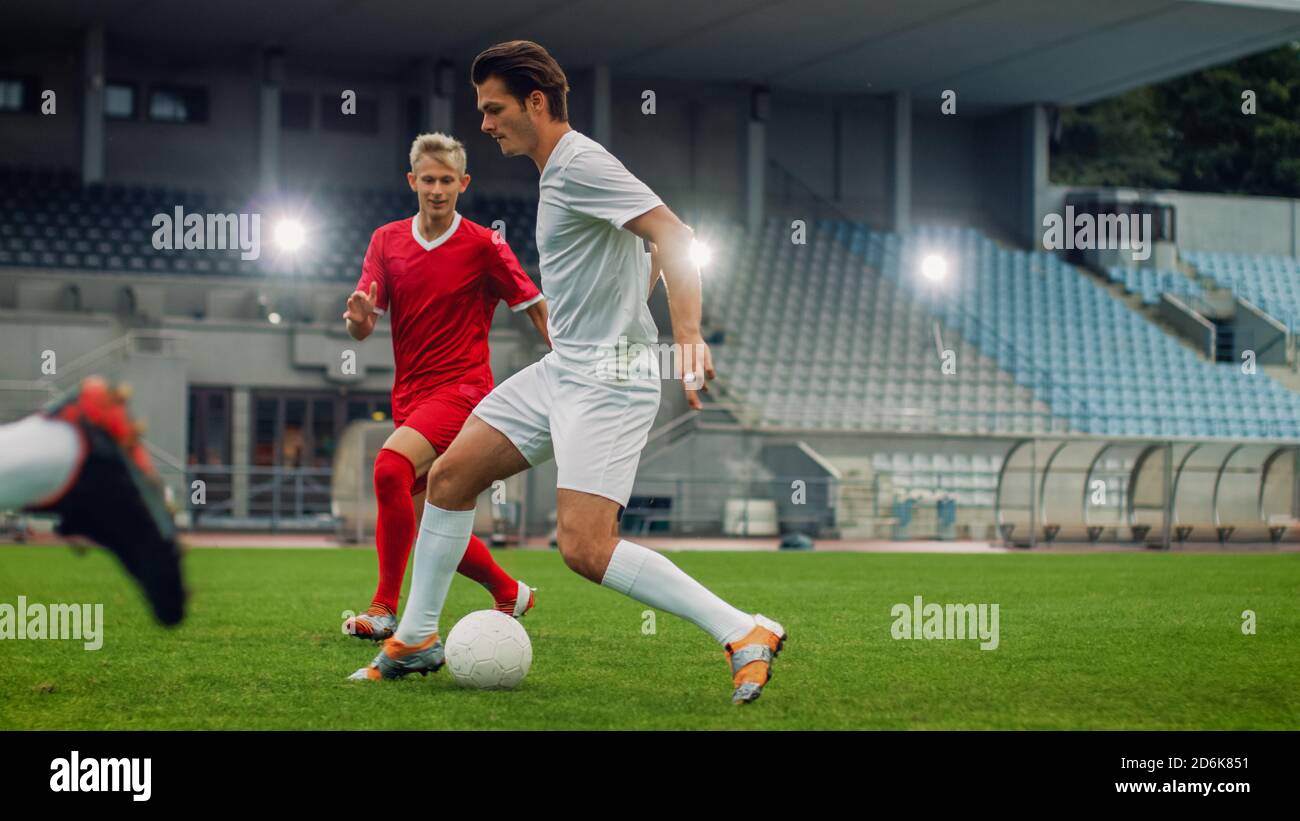 Professional Soccer Player Leads with a Ball, Masterfully Dribbling and Bypassing Sliding Tackles of His Opponents. Two Professional Football Teams Stock Photo