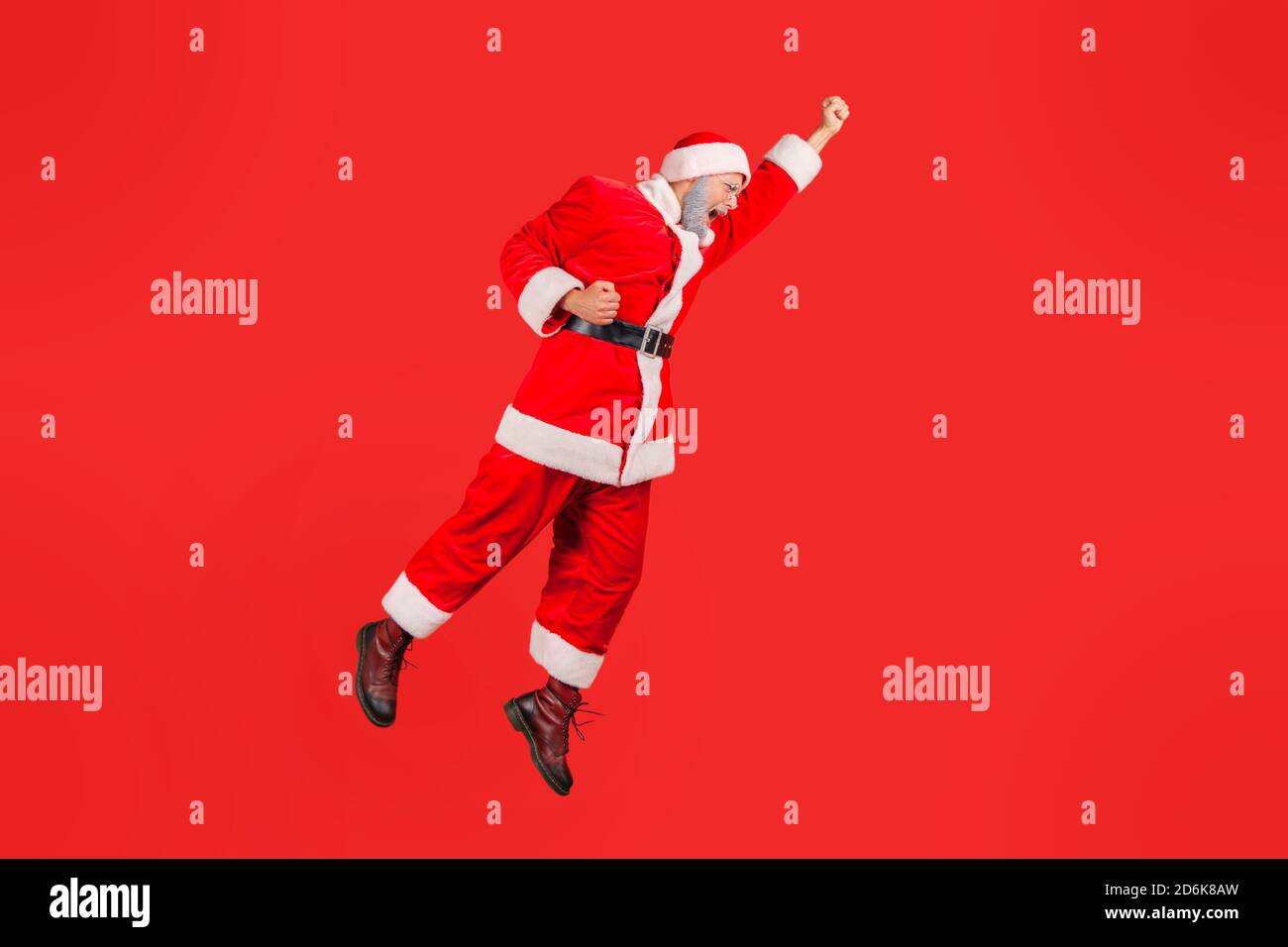 Full length cheerful positive santa claus jumping high and flying in the air like superhero, in hurry to celebrate winter holidays. Indoor studio shot Stock Photo