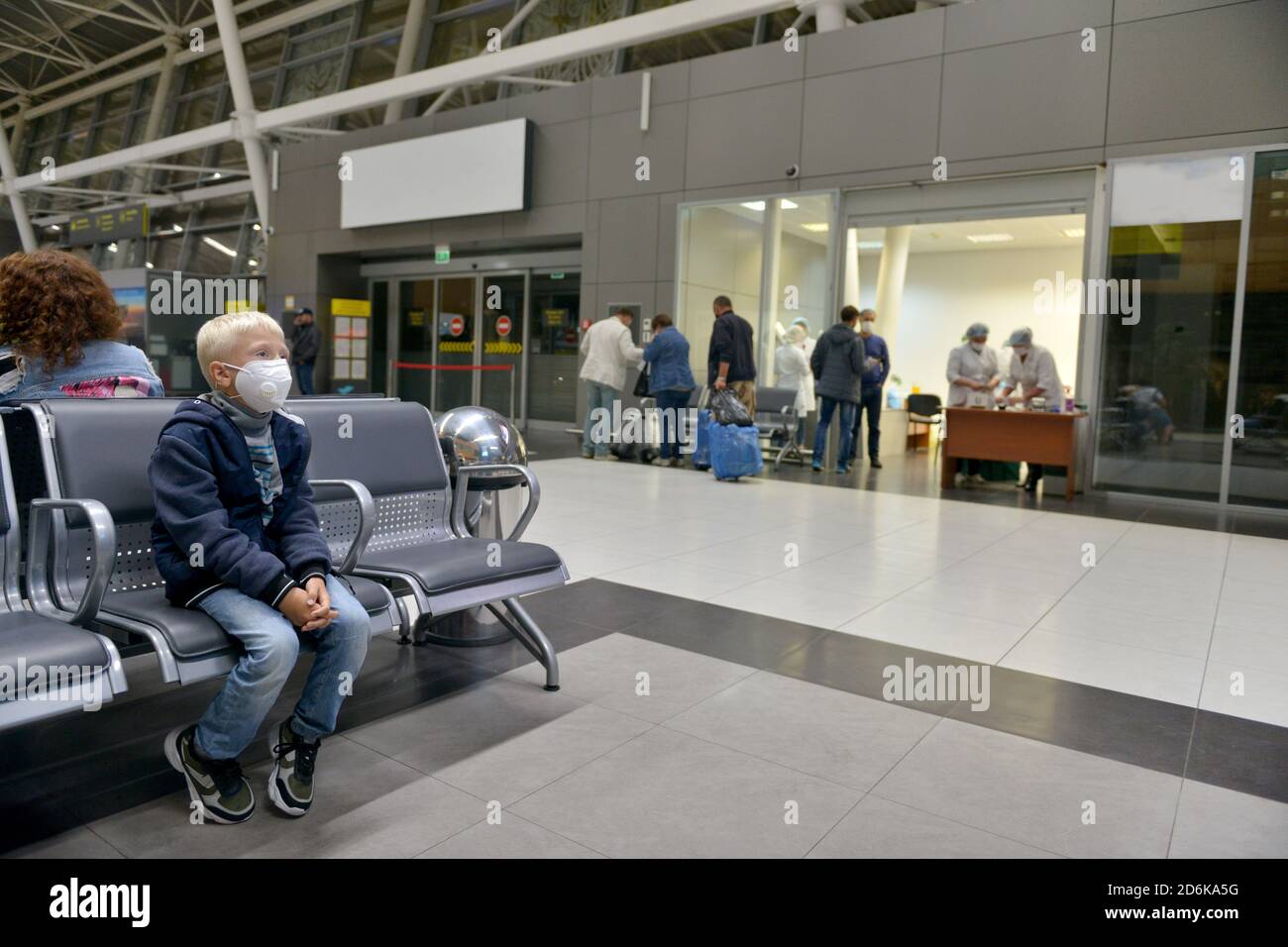The boy is sitting at the airport in a medical mask. Children wear a face mask during a coronavirus and flu outbreak. Protection from viruses Stock Photo