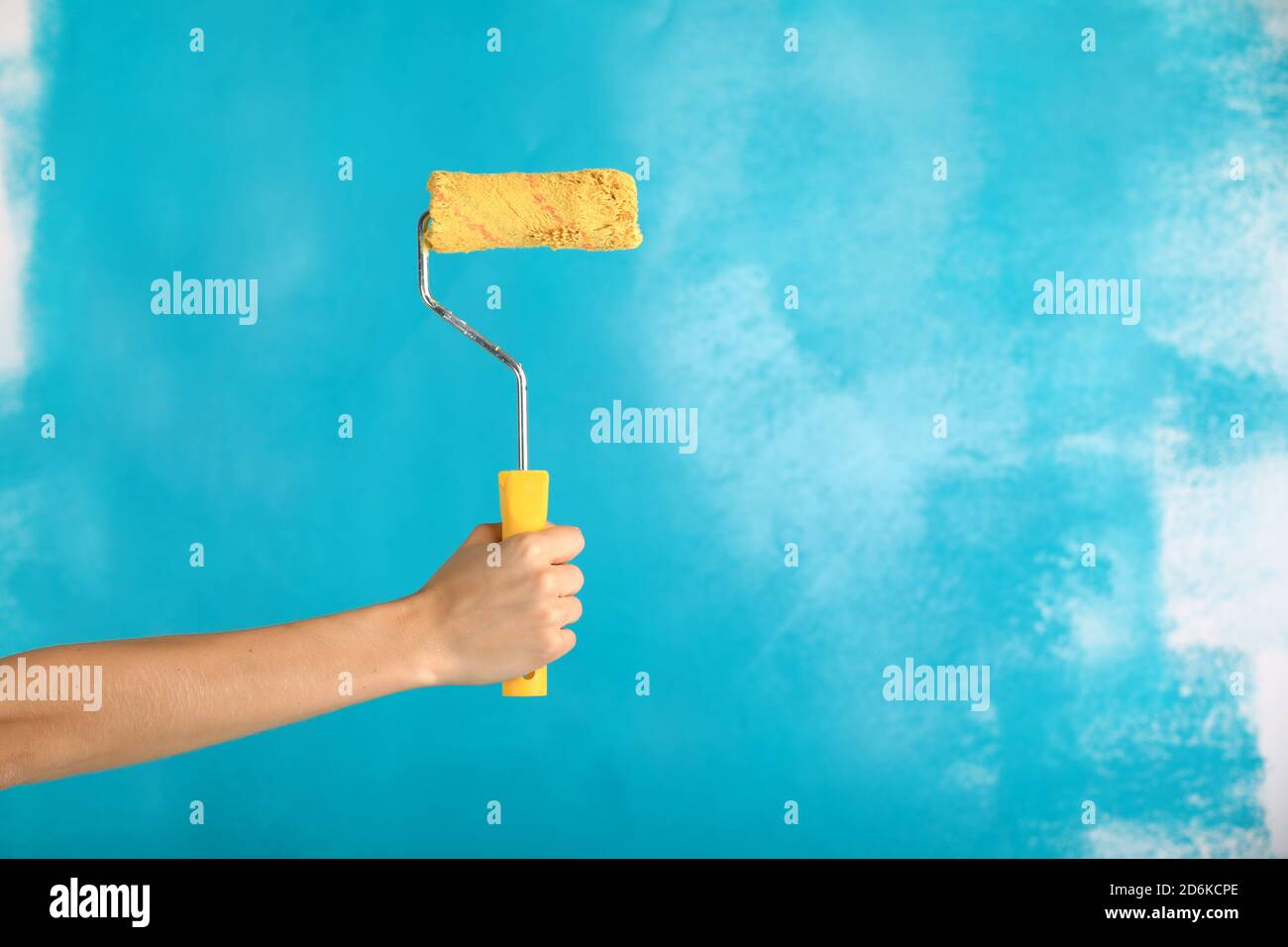 close up of female hand holding paint yellow roller over blue background-repair, construction and building tools concept. Convenient and versatile Stock Photo
