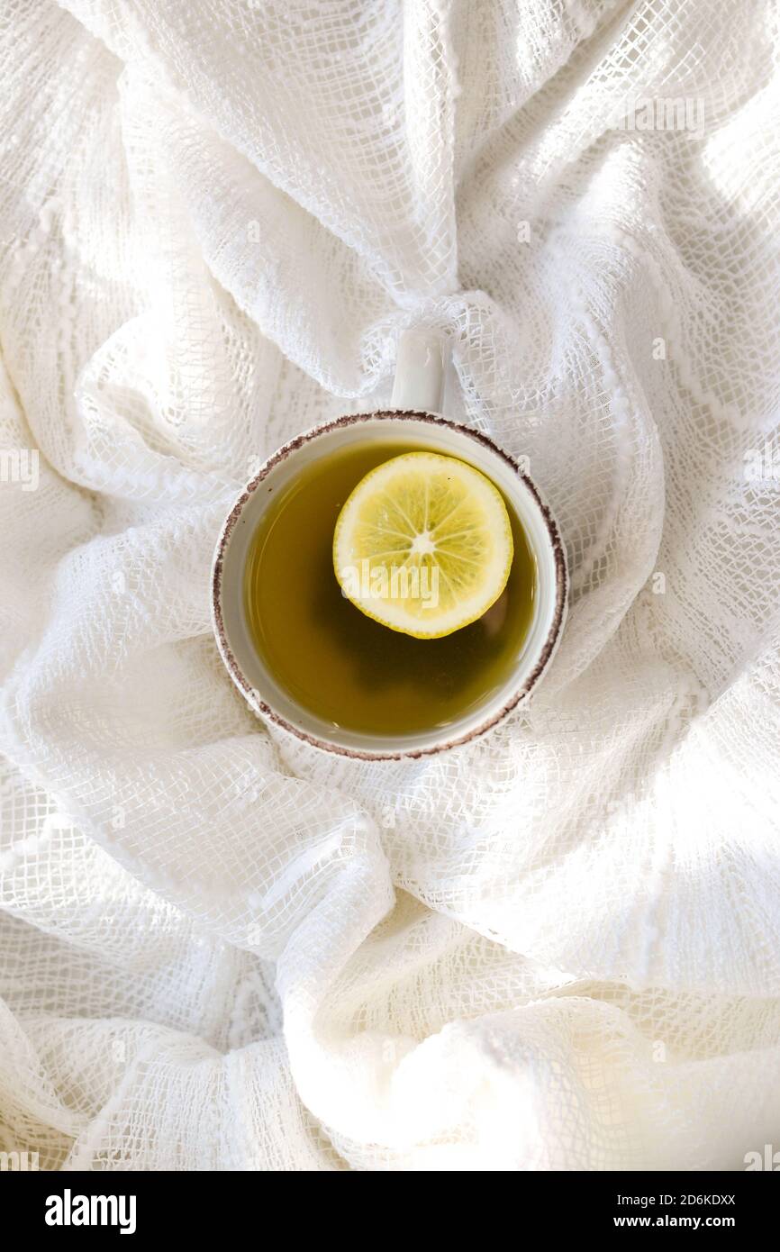 A cup with tea and lemon. Top view. White background. A cup on a white bed, sunbeams. Stock Photo