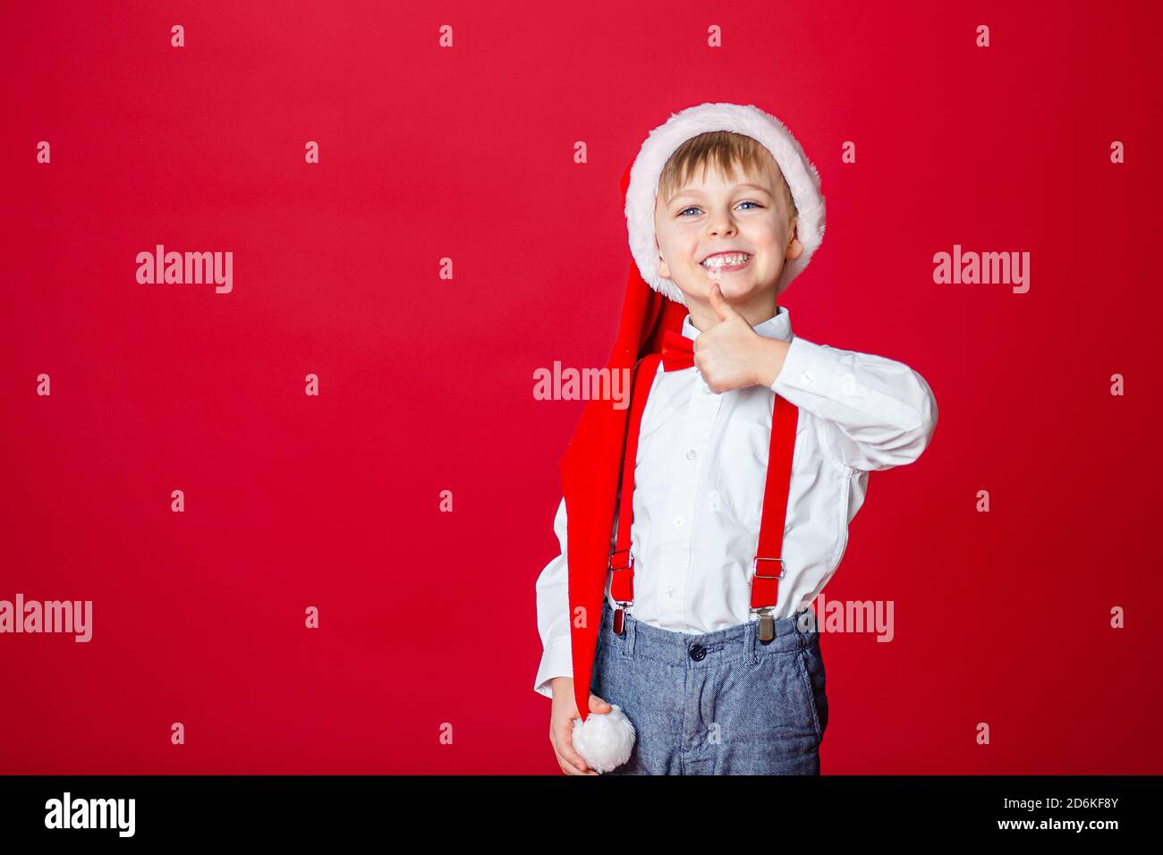 Merry Christmas. Cute cheerful little boy in Santa Claus hat on red background. A happy childhood with dreams and gifts. Close-up of baby's open mouth Stock Photo
