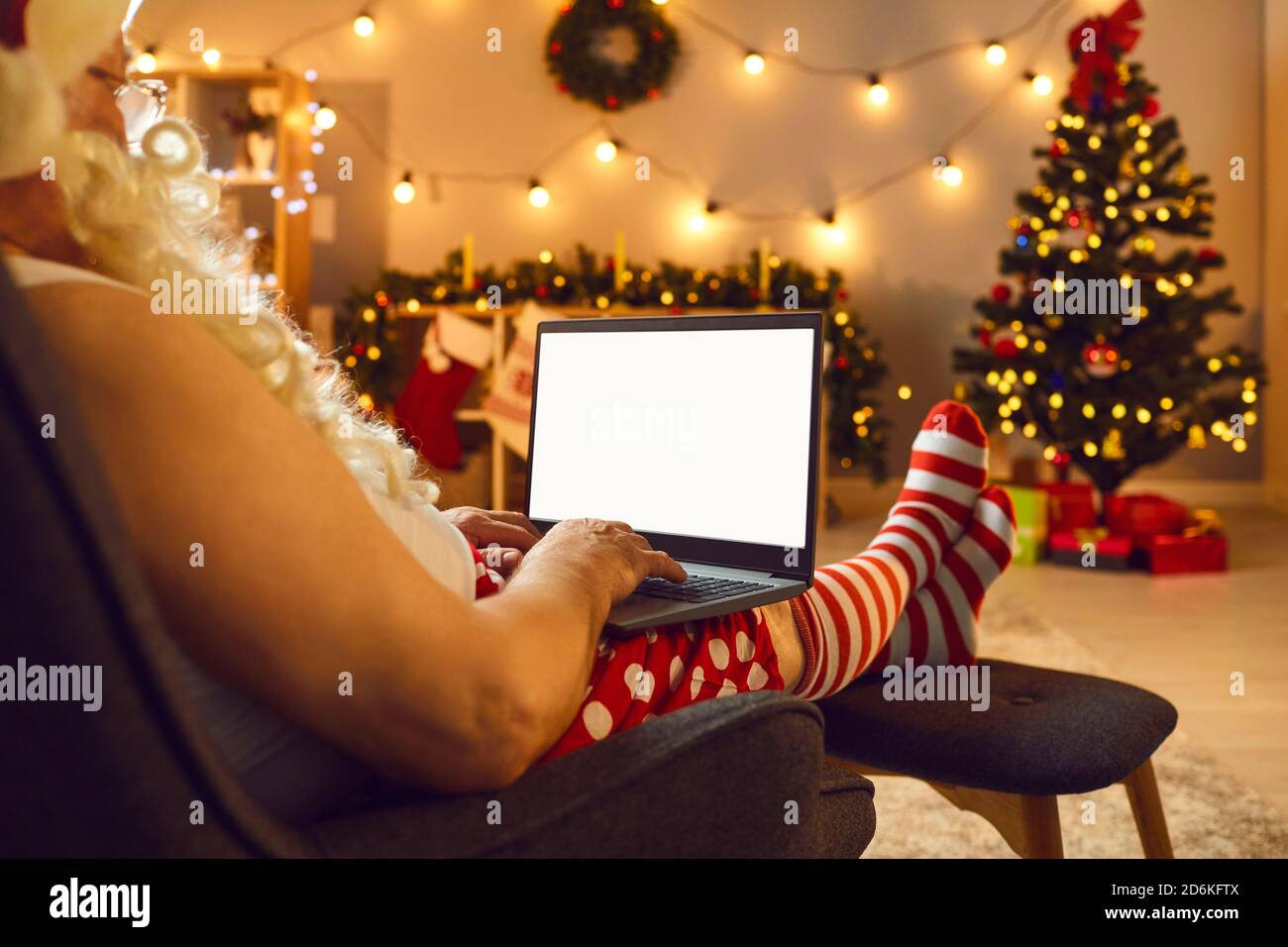 Santa in costume with white beard communicating online on laptop with space for text on screen Stock Photo