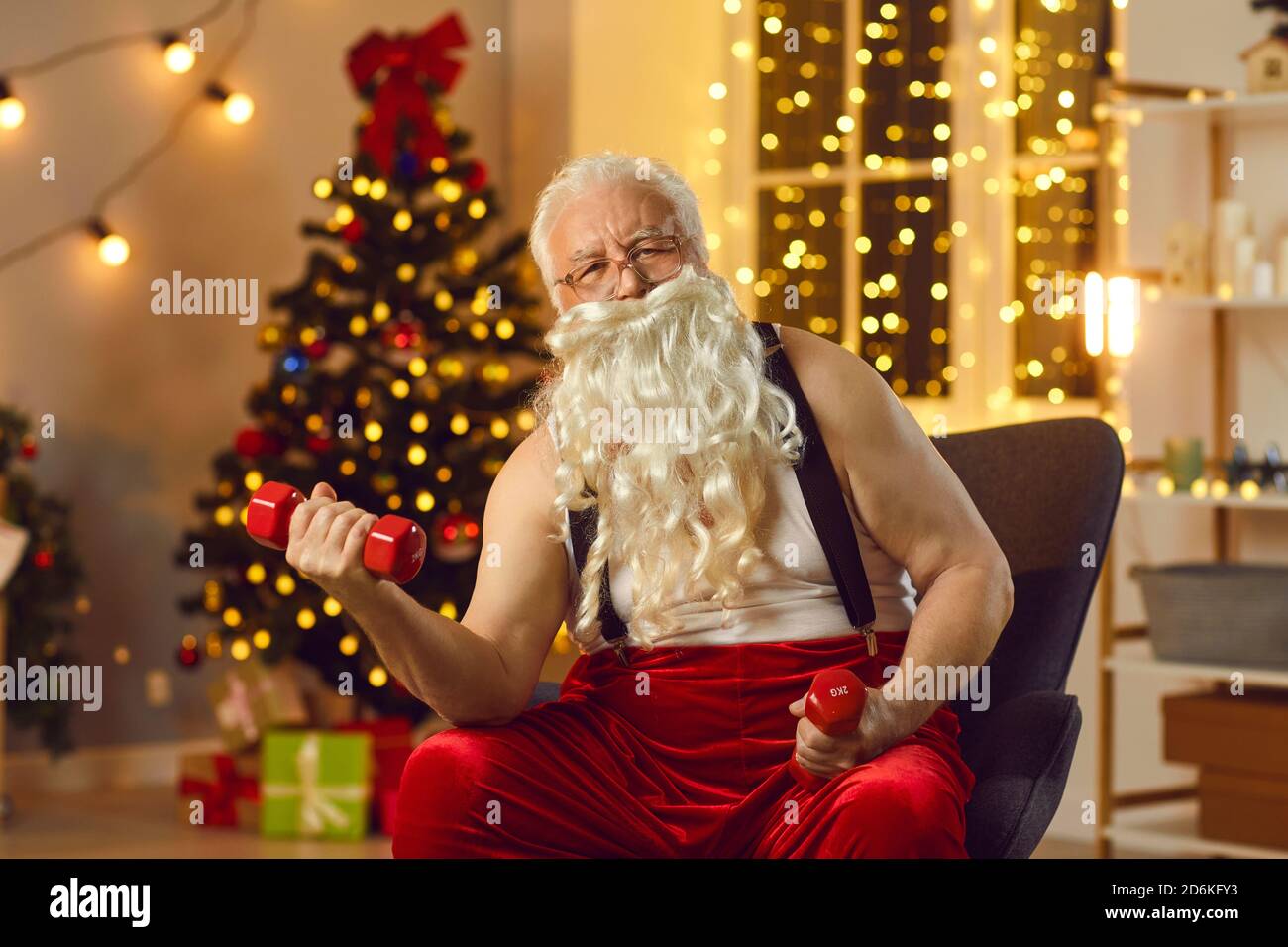 Elderly funny Santa in red velvet suspender costume making exercise with dumbbels Stock Photo