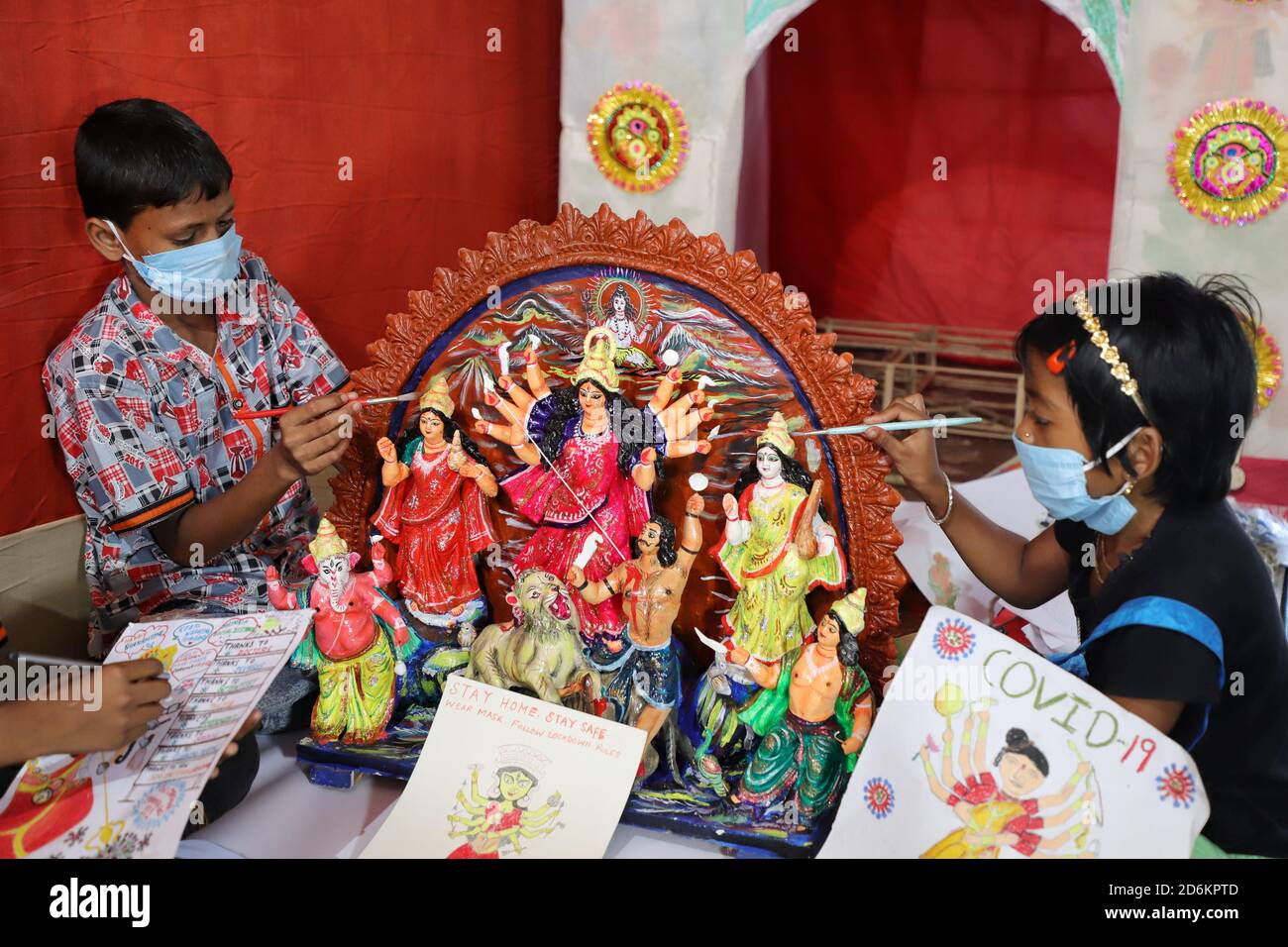 Children from Sundarbans wearing face masks paint and give finishing touches to a 1.5 feet tall clay idol of Goddess Durga prior to the Durga puja festival amidst Covid-19 pandemic. Stock Photo
