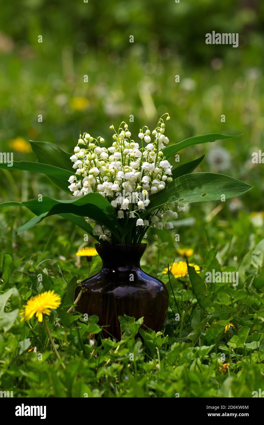 Vertical shot of a vase with lilies of the valley on blurred background ...