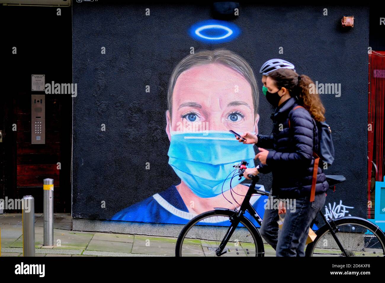 Young couple with bicycle in a black face masks passing by the mural in the High street, Manchester. Nurse Debra Williams as an angel by AKSE. New str Stock Photo