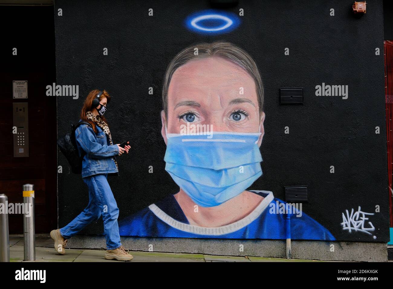 Young woman in a black face mask passing by the mural in the High street, Manchester. Nurse Debra Williams as an angel by AKSE. New street art celebra Stock Photo