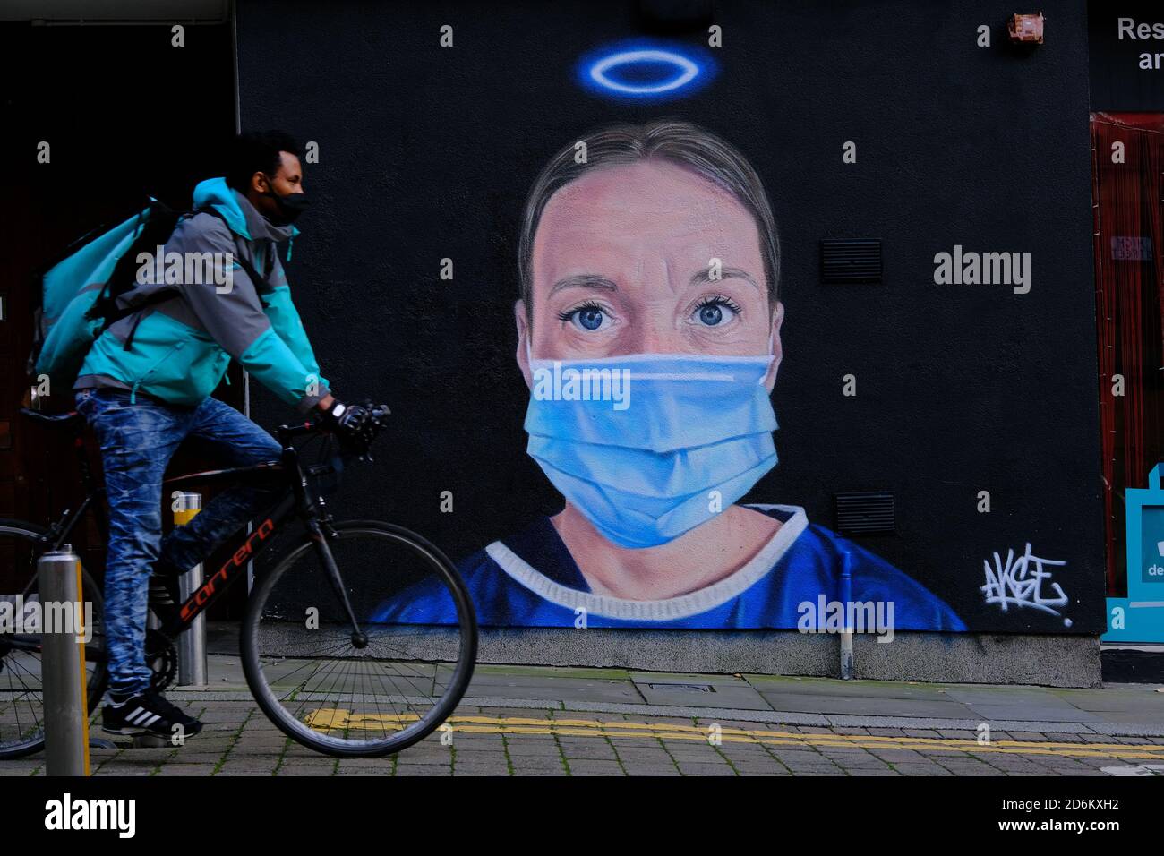 Young man on bicycle in a black face masks passing by the mural in the High street, Manchester. Nurse Debra Williams as an angel by AKSE. New street a Stock Photo