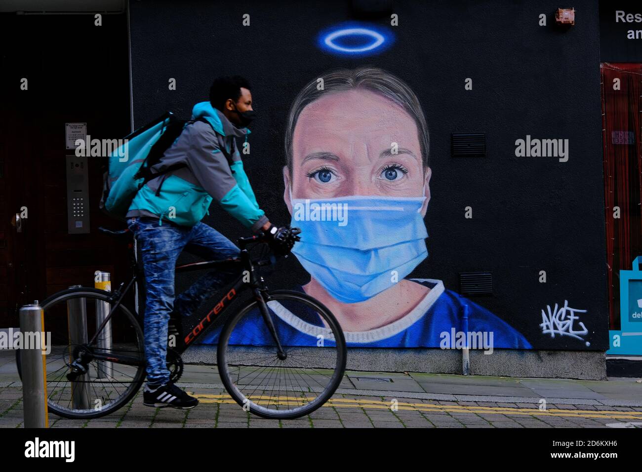Young man on bicycle in a black face masks passing by the mural in the High street, Manchester. Nurse Debra Williams as an angel by AKSE. New street a Stock Photo