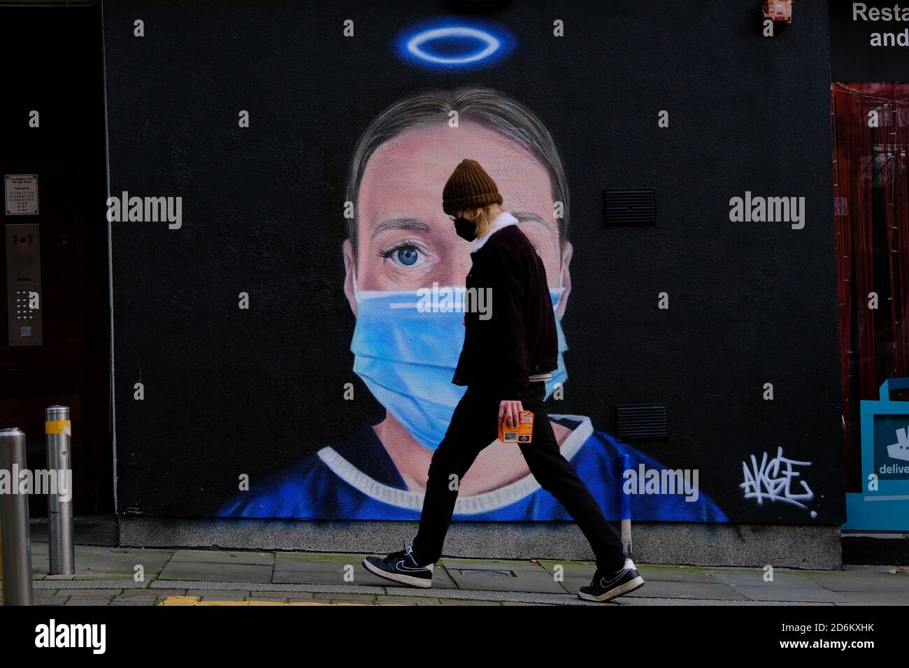 Young sad man in a black face masks passing by the mural in the High street, Manchester. Nurse Debra Williams as an angel by AKSE. New street art cele Stock Photo