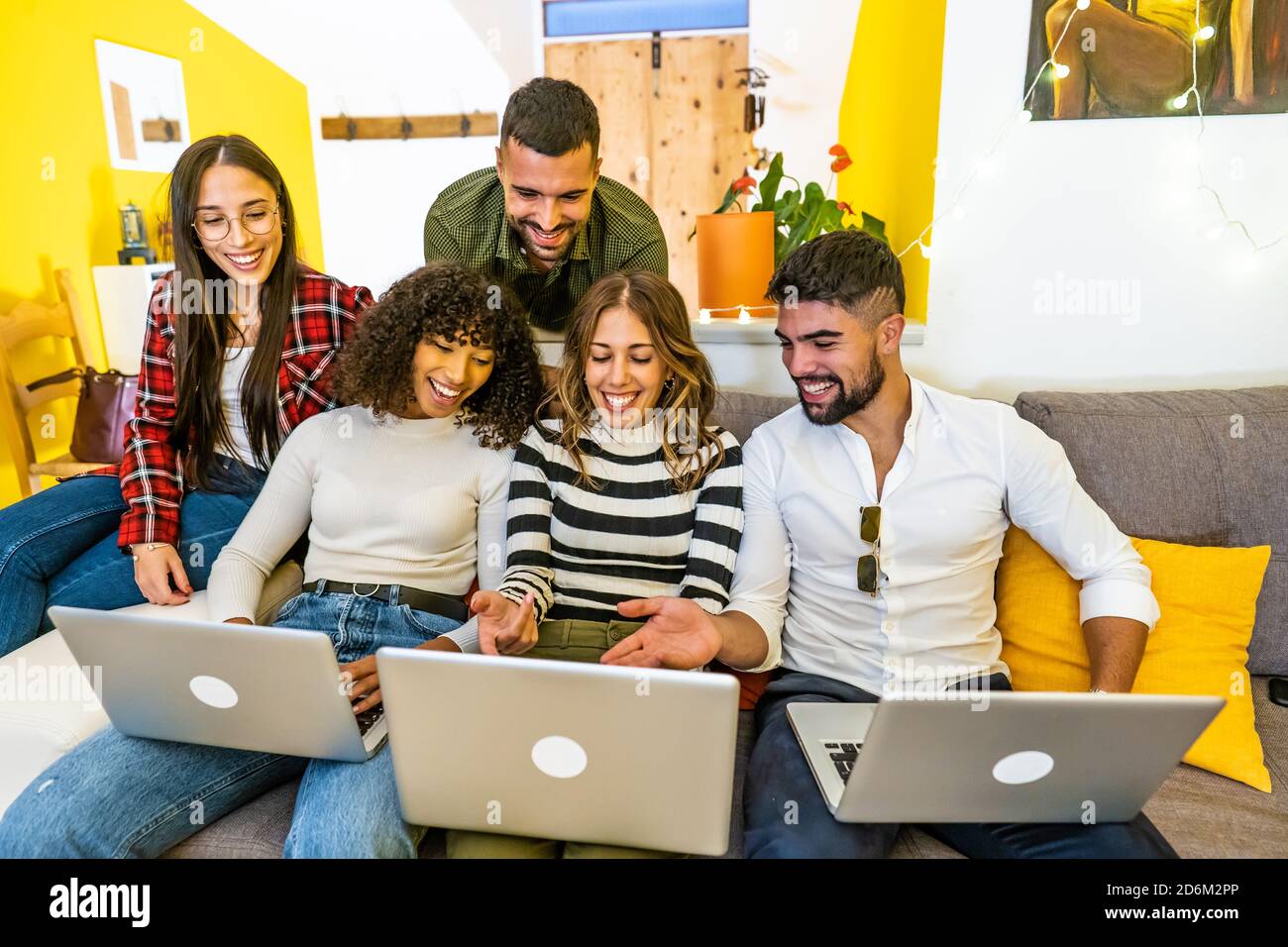 Mixed race happy friends group using three laptops at home on the sofa - Young people having fun together with social network looking at the computer Stock Photo
