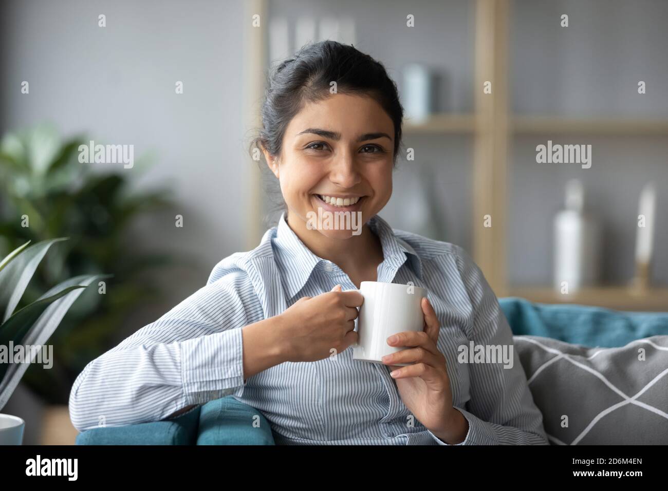 Attractive Indian girl sit on couch with cup of tea Stock Photo