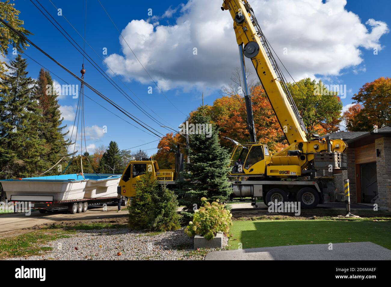 Crane ready to lift fiberglass swimming pool shell from flatbed truck over hydro wires and house to back yard in the Fall Stock Photo