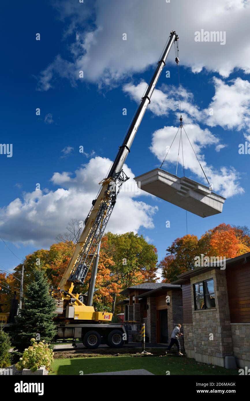 Tall crane lifting fiberglass swimming pool shell over a house to back