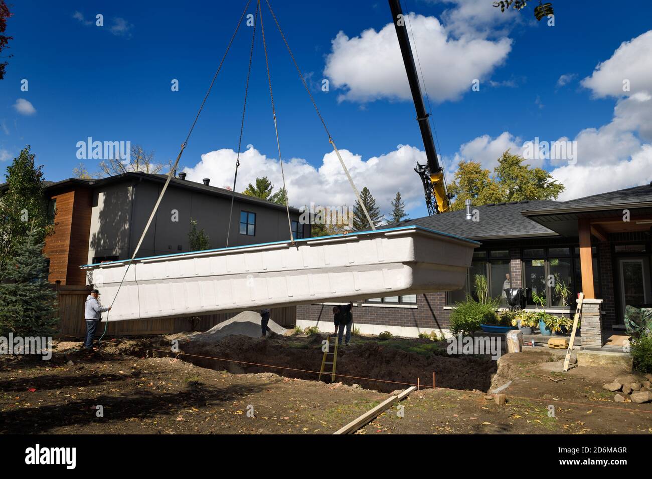 Crane lifting a fiberglass swimming pool shell into a hole dug in the