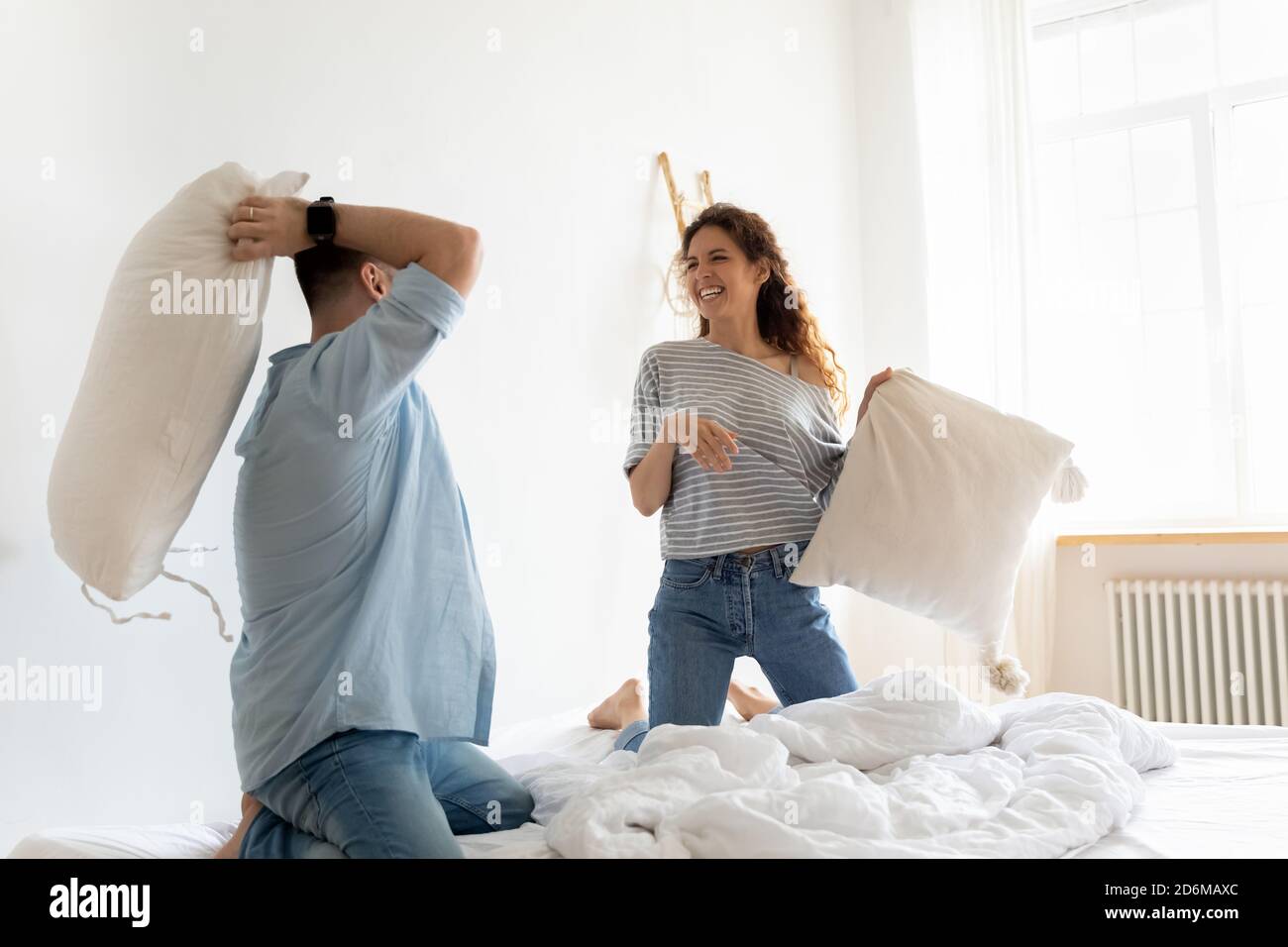 Happy laughing young couple playing pillow fight in bedroom Stock Photo