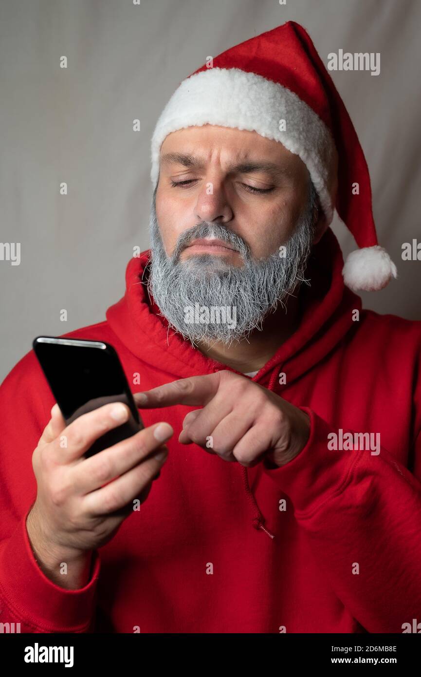 Santa Claus types something on his cell phone and looks suspicious Stock Photo