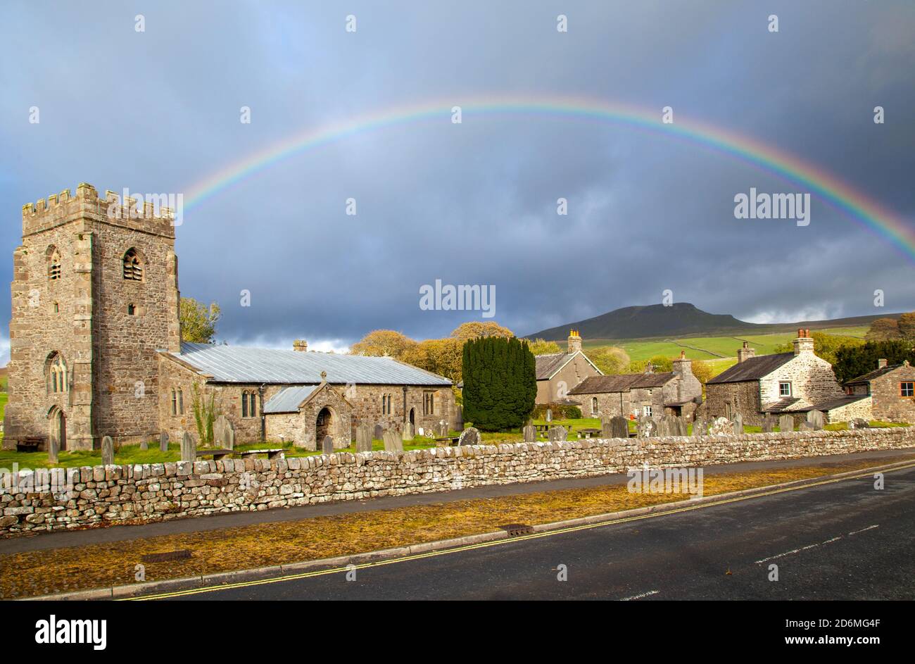 Rainbow over the village church of St Oswalds in the Yorkshire village of Horton in Ribblesdale with the mountain of Pen-y-ghent  on the Pennine Way Stock Photo