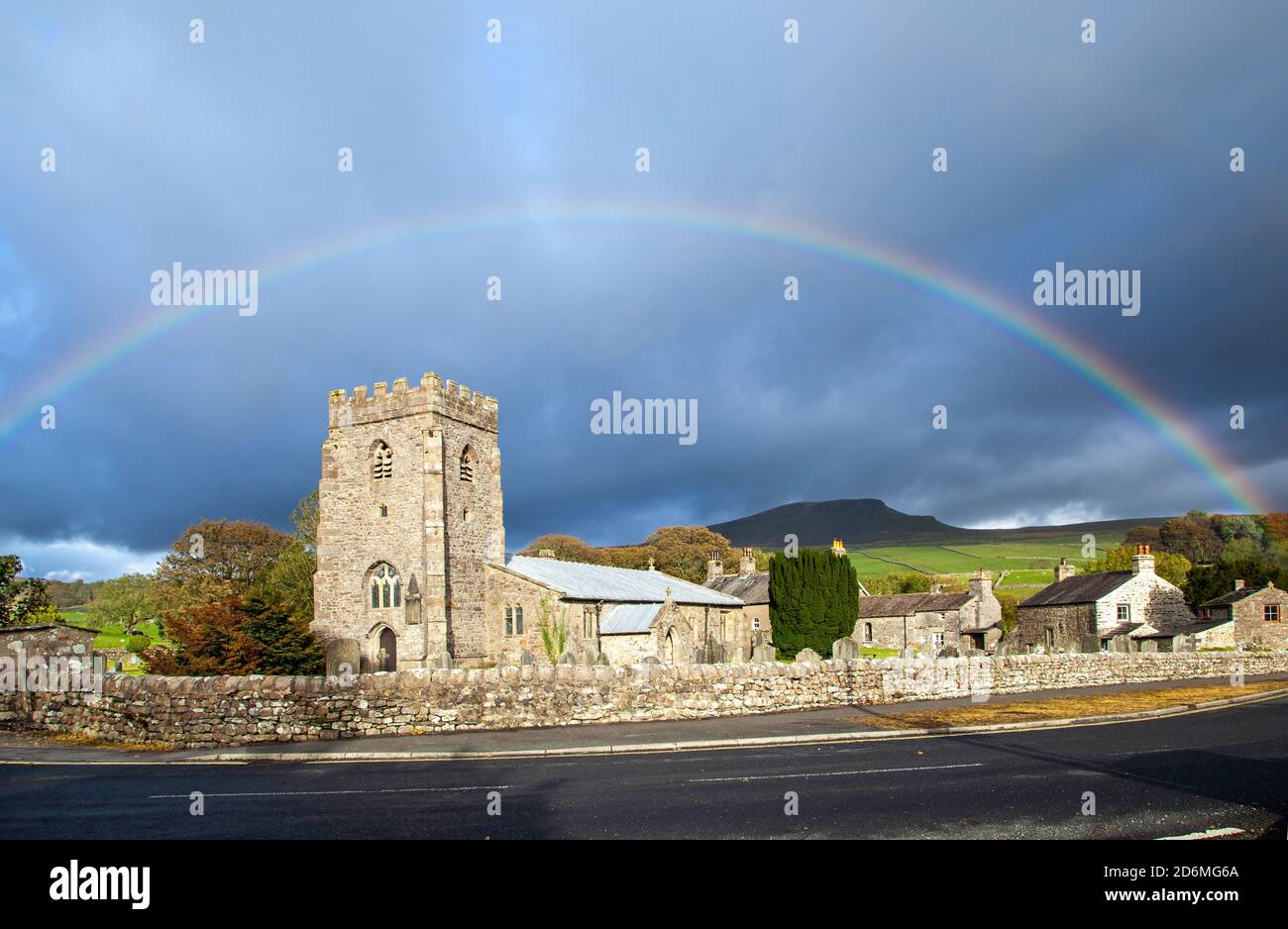 Rainbow over the village church of St Oswalds in the Yorkshire village of Horton in Ribblesdale with the mountain of Pen-y-ghent  on the Pennine Way Stock Photo