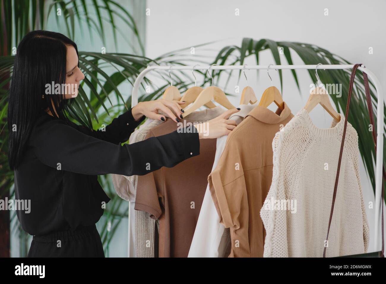 Young brunette woman choosing clothes on a rack in a modern showroom. Stock Photo