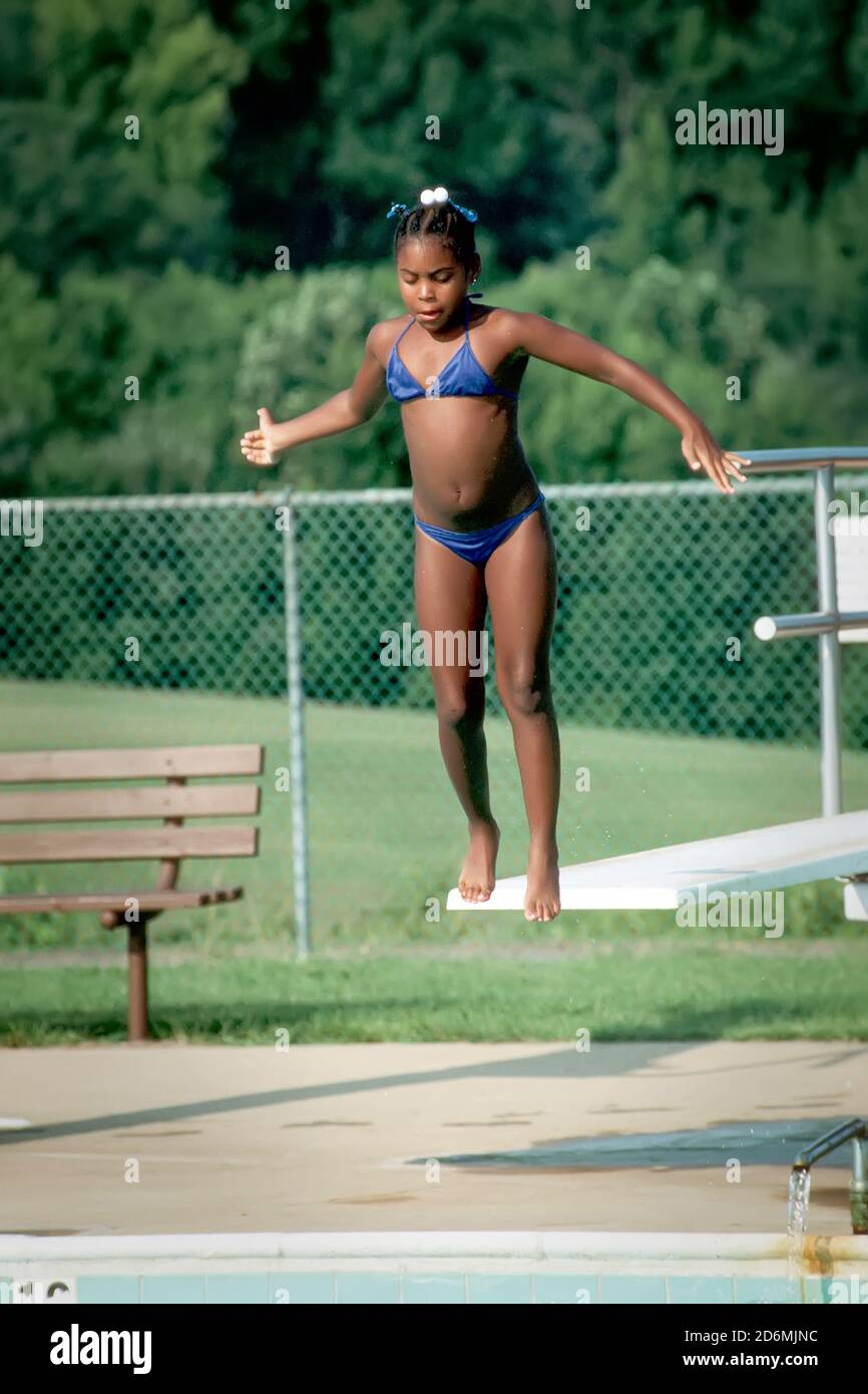 A young black female jumps off of a diving board at a public swimming pool Stock Photo