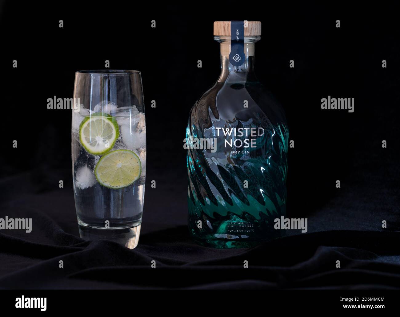 Still life of Twisted Nose gin brand bottle and glass with tonic, ice and lime on black velvet background Stock Photo