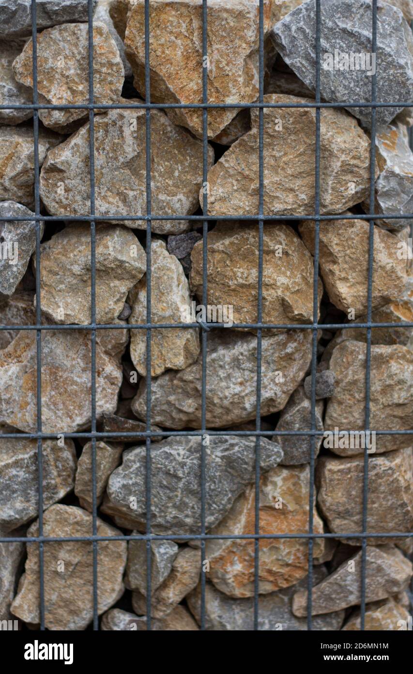 A fragment of wall made of wired cage filled with stones . Gabion wire