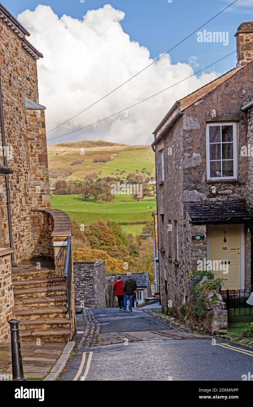 People walking up the street of Mill Brow in the cumbrian  market town of Kirkby Lonsdale with a view of the Yorkshire Dales beyond Stock Photo