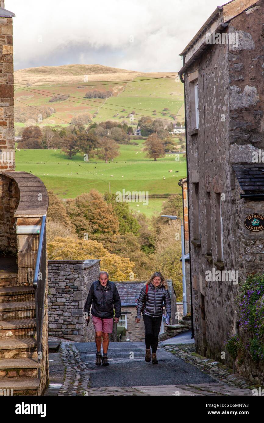 People walking up the street of Mill Brow in the cumbrian  market town of Kirkby Lonsdale with a view of the Yorkshire Dales beyond Stock Photo
