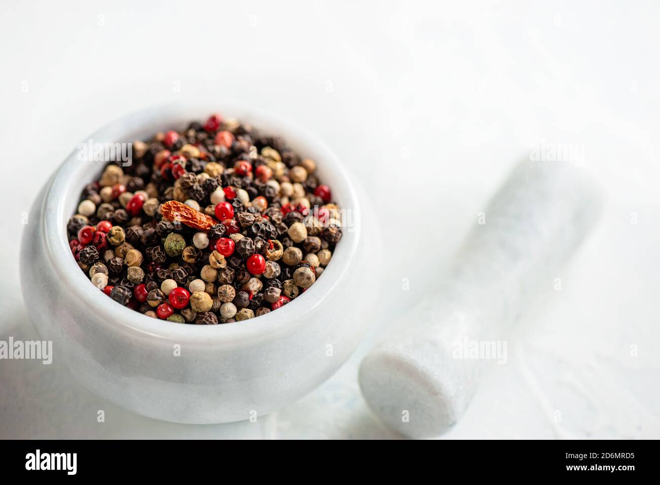 White porcelain mortar and pestle with hot red chili pepper and different types of peppers