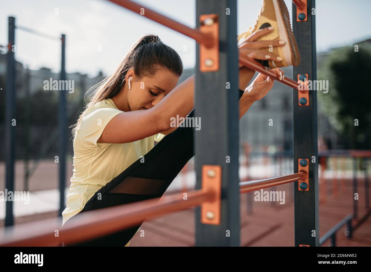 Strong young woman stretching legs near wall bar Stock Photo