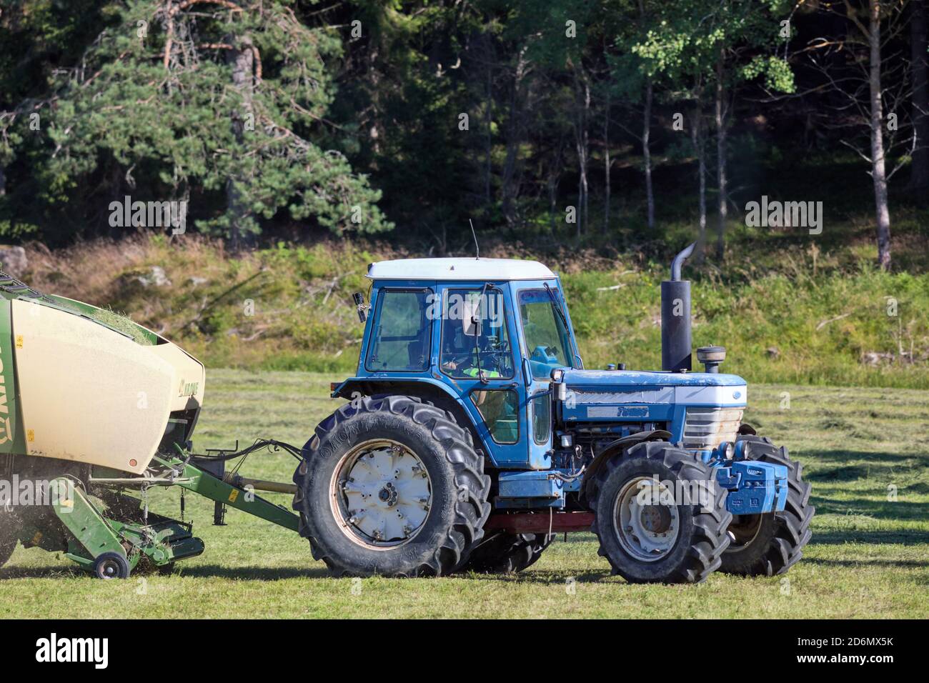 Blue Ford tractor reaping harvest near Söderby, Bogesundslandet, near Vaxholm, Sweden Stock Photo