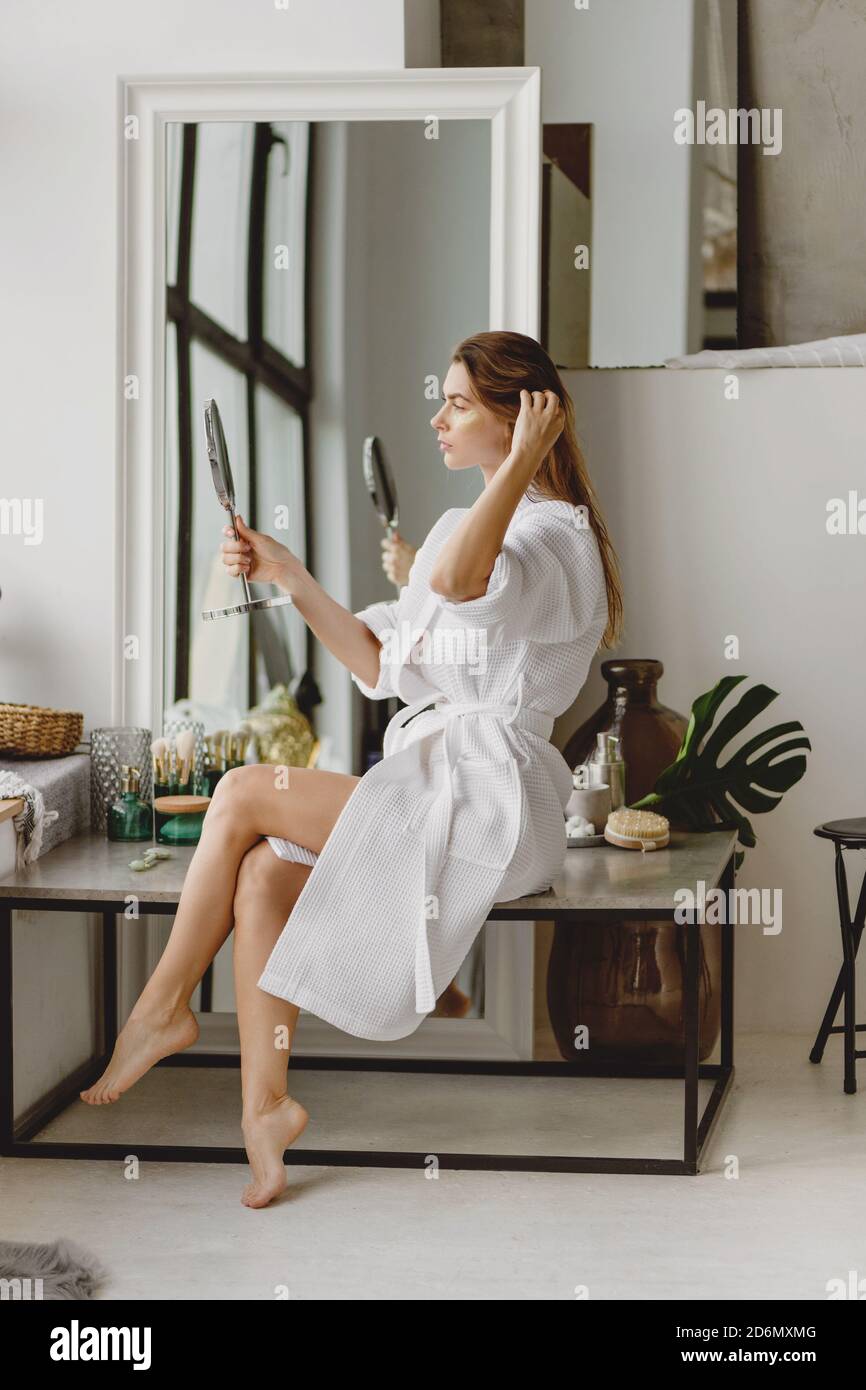 Beautiful long-haired woman in white bathrobe doing makeup in the morning. Stock Photo