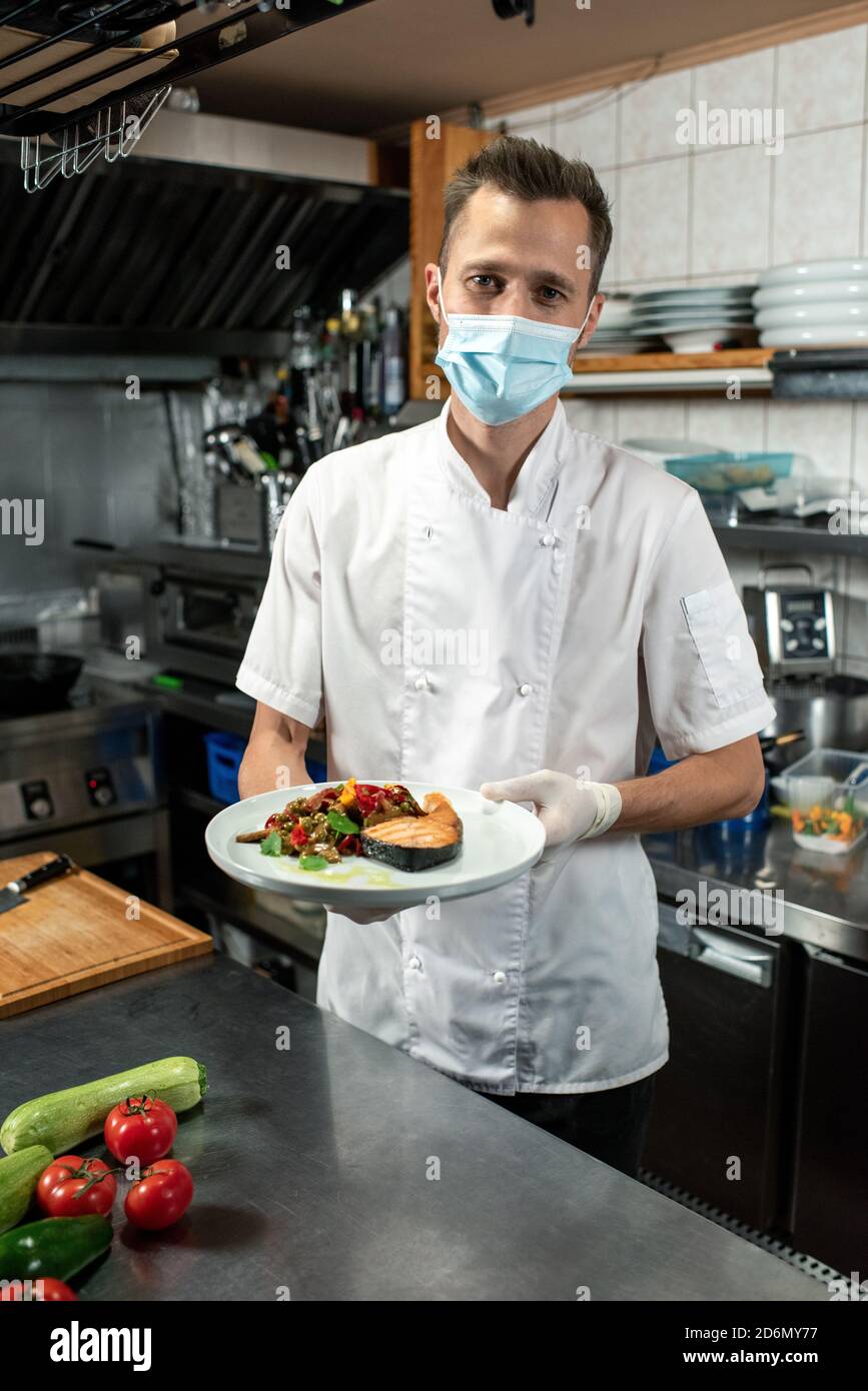 Male chef holding fried salmon with steamed vegetables over kitchen table Stock Photo