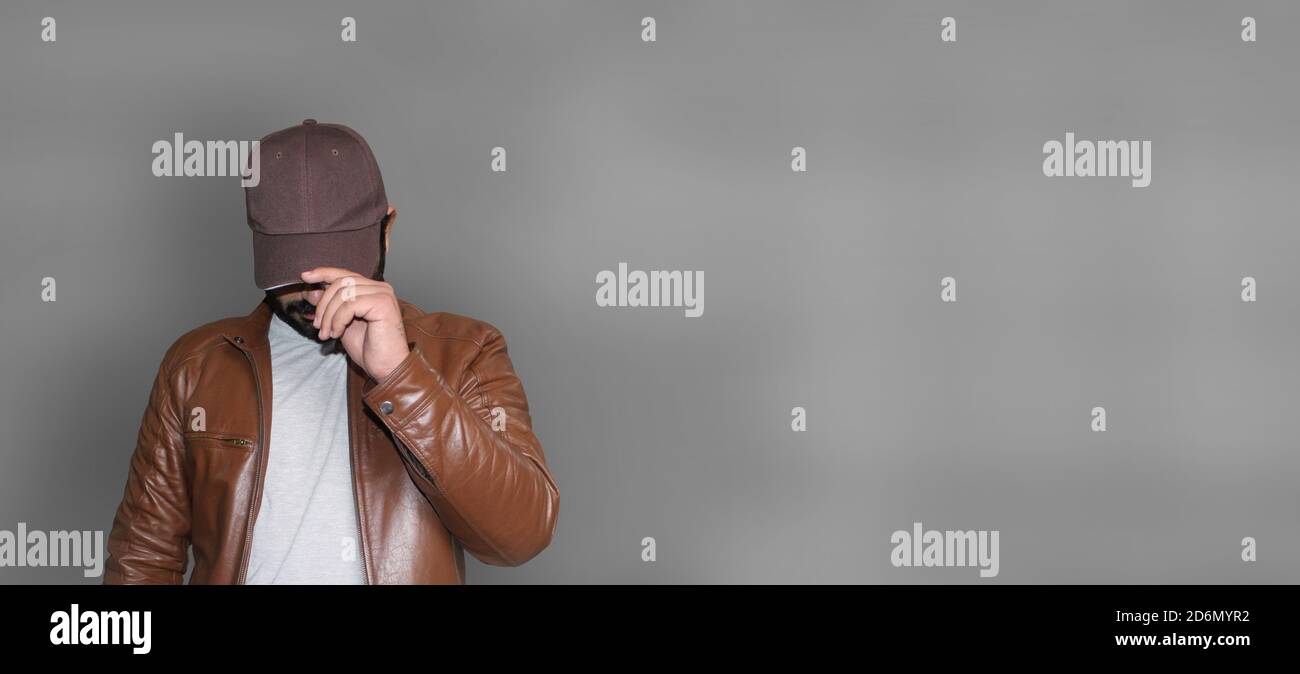 Handsome young man wearing brown leather jacket hiding his face behind the Cap. Stock Photo