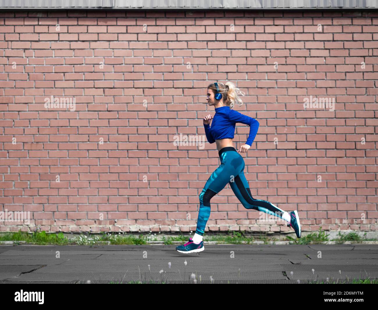Woman jogging outdoor in a sunny day. Sport and healthy lifestyle concept. Brick wall background. Stock Photo