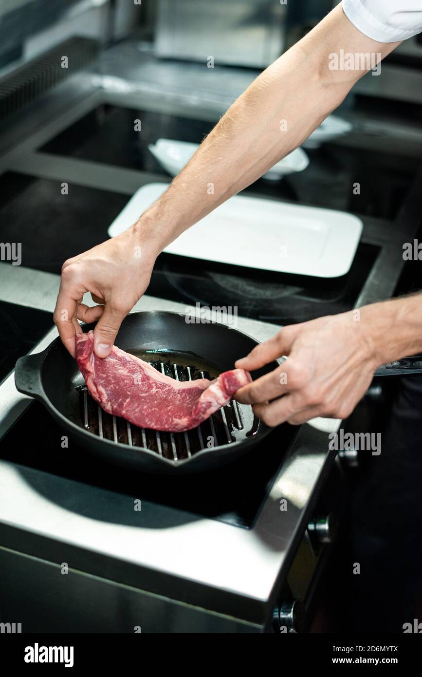 Hands of young chef putting piece of meat on grill frying pan with vegetable oil Stock Photo