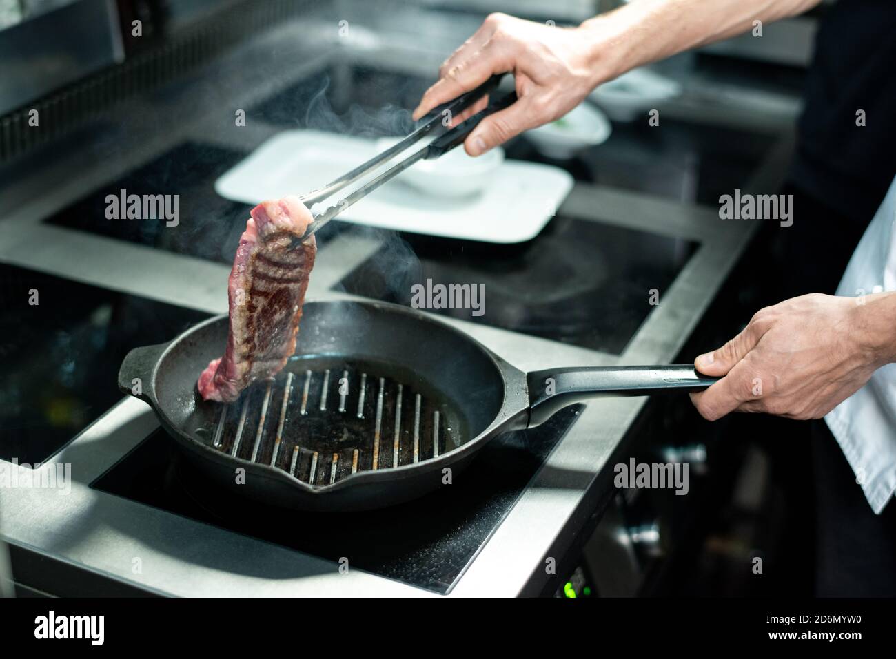 Hands of young chef holding halfroasted piece of meat over hot grill