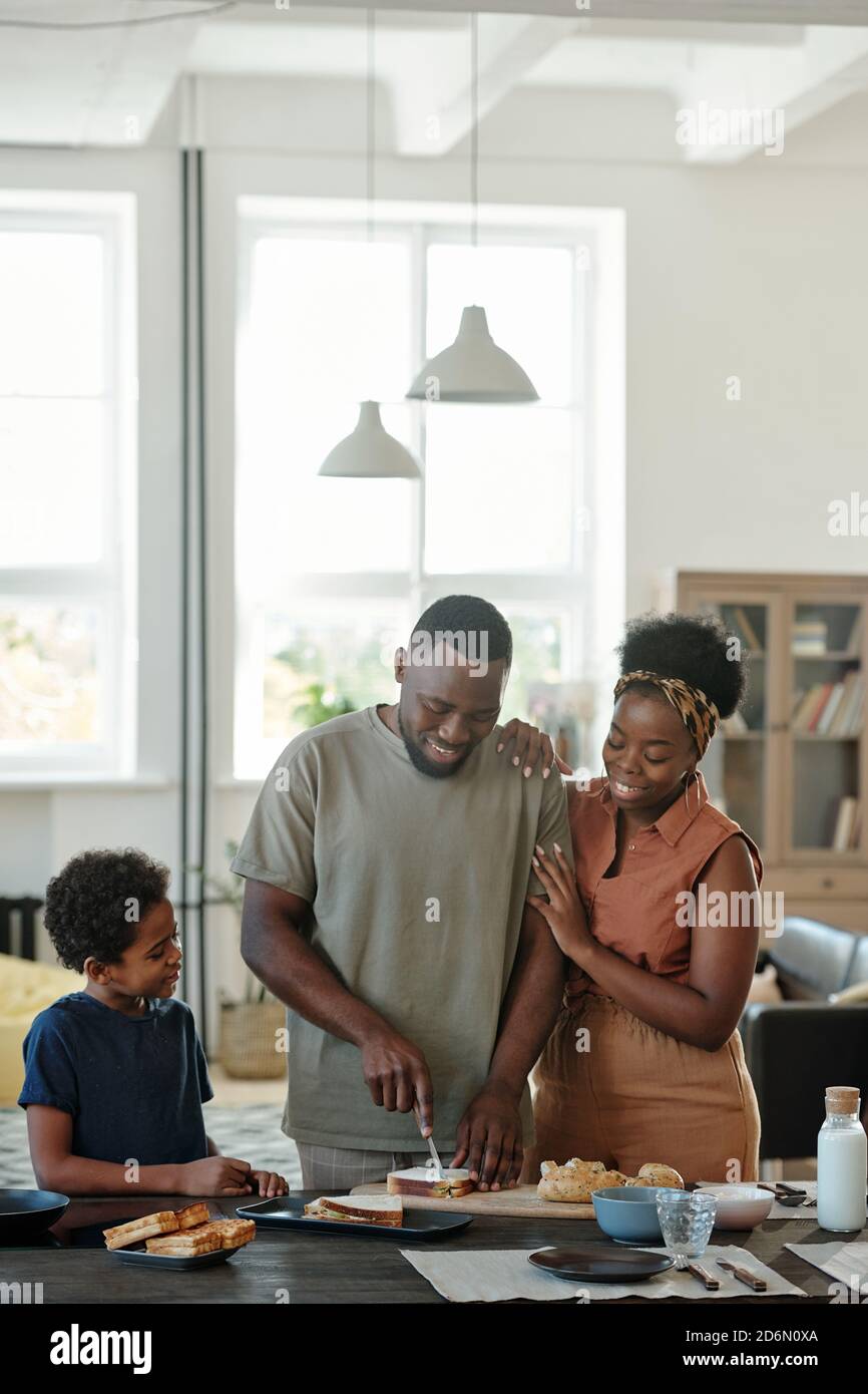 Young African man cutting bread while preparing sandwiches for his