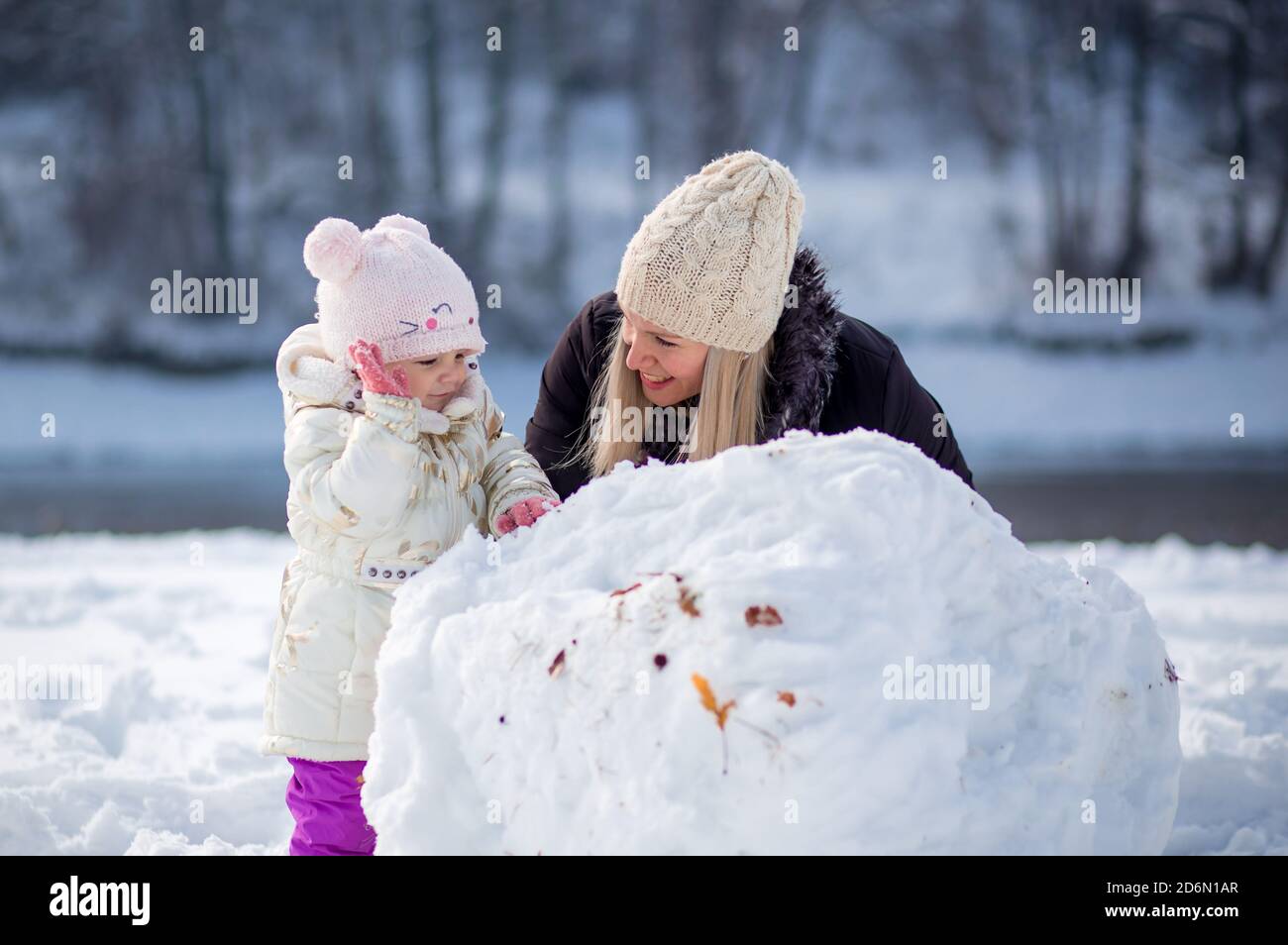 Young mom plays outiside with her daughter. Making snowman Stock Photo